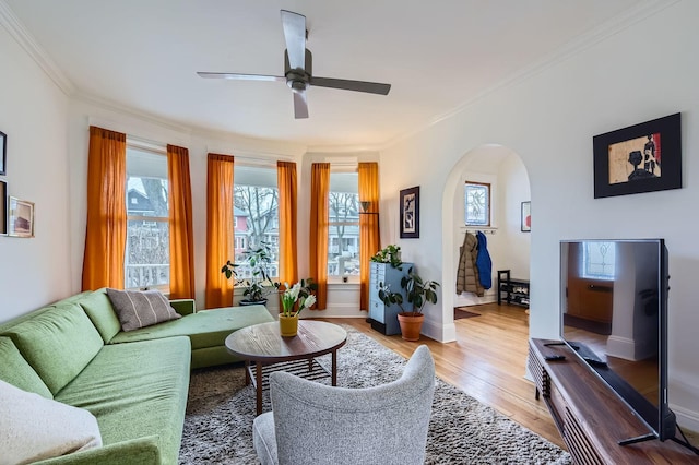 living room with arched walkways, crown molding, light wood-style floors, a ceiling fan, and baseboards