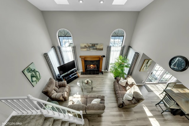 living room with a high ceiling, a premium fireplace, a skylight, and light wood-style flooring