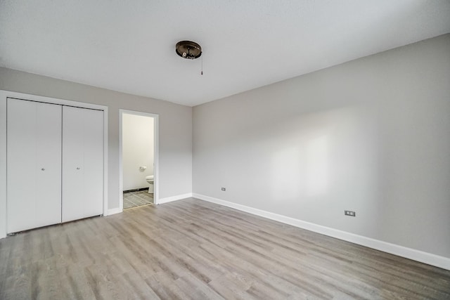 unfurnished bedroom featuring light wood finished floors, a closet, ensuite bath, and baseboards