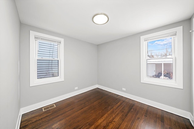 empty room with dark wood-style flooring, visible vents, and baseboards