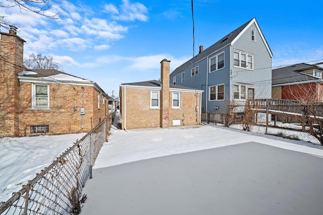 snow covered rear of property featuring a chimney, fence, and brick siding