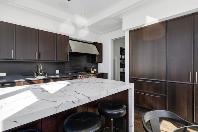 kitchen featuring a breakfast bar area, backsplash, a sink, wall chimney range hood, and range