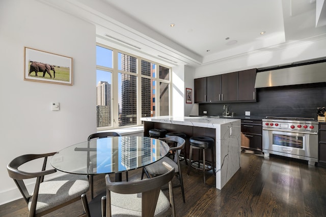 kitchen with a city view, a kitchen island, dark brown cabinets, ventilation hood, and premium stove