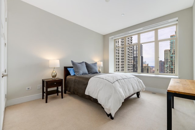 bedroom with a view of city, light carpet, and baseboards