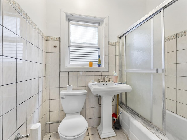 bathroom with toilet, bath / shower combo with glass door, and tile walls