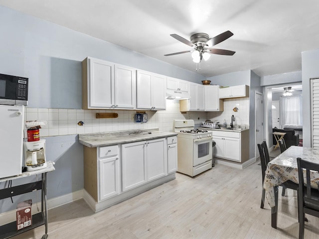 kitchen with light countertops, stainless steel microwave, white cabinets, white range with gas cooktop, and a sink