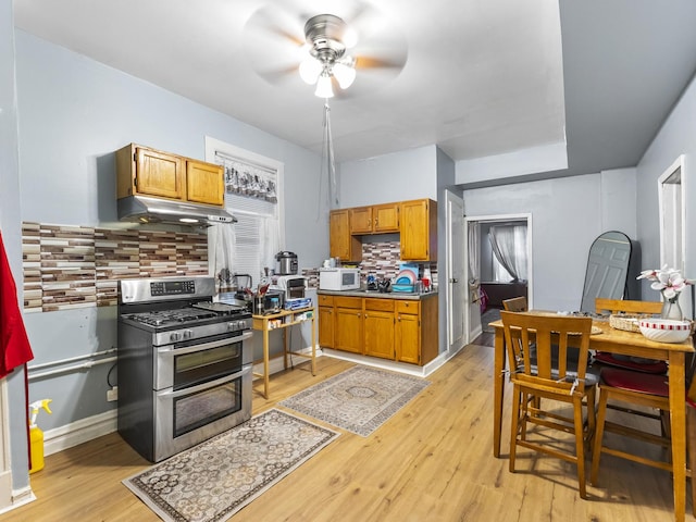 kitchen featuring light wood-style floors, white microwave, under cabinet range hood, double oven range, and backsplash