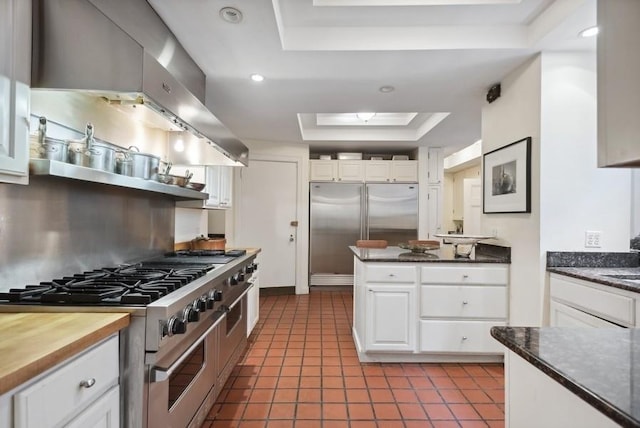 kitchen featuring a raised ceiling, high quality appliances, extractor fan, dark tile patterned floors, and white cabinetry