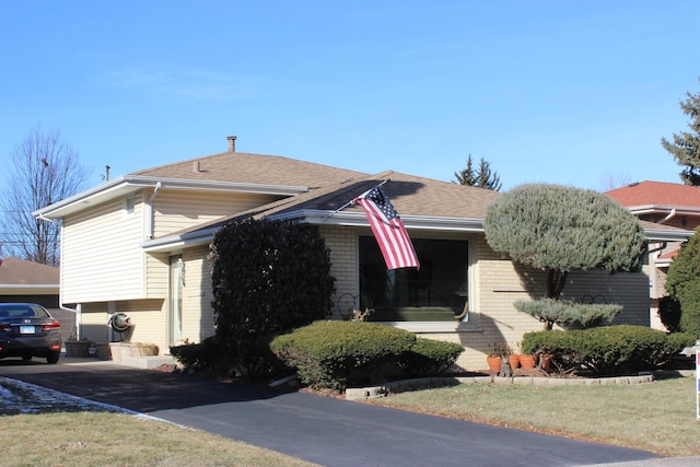 view of front facade featuring brick siding, roof with shingles, and a front lawn