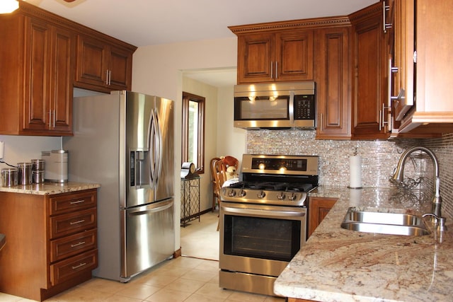 kitchen featuring light tile patterned floors, stainless steel appliances, backsplash, a sink, and light stone countertops