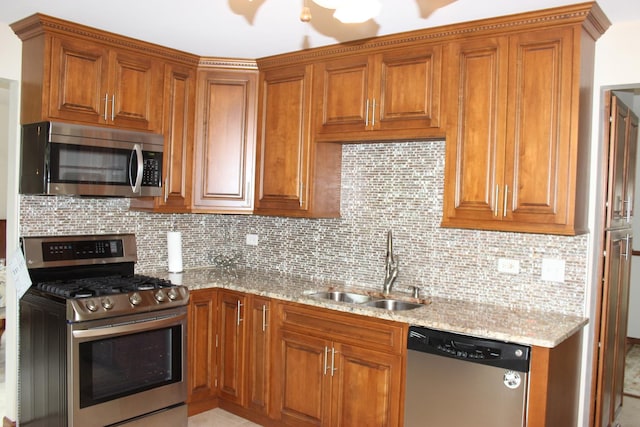 kitchen with brown cabinets, appliances with stainless steel finishes, a sink, and light stone countertops