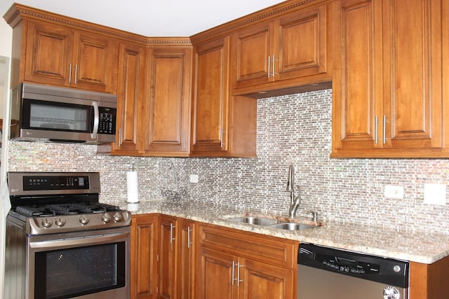 kitchen featuring light stone countertops, stainless steel appliances, a sink, and brown cabinetry