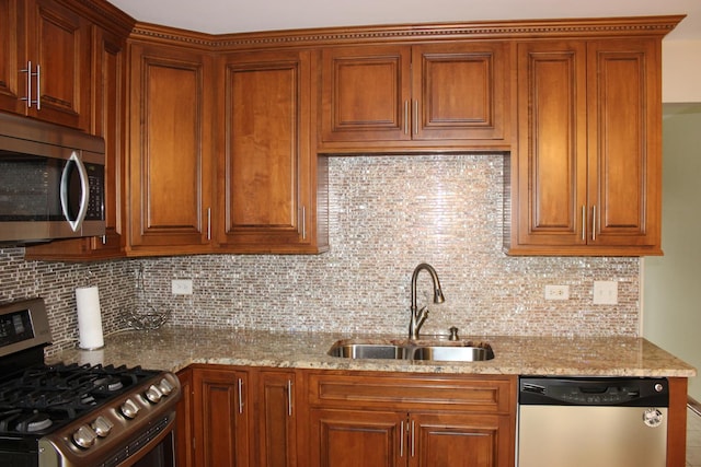 kitchen with light stone counters, a sink, appliances with stainless steel finishes, tasteful backsplash, and brown cabinetry