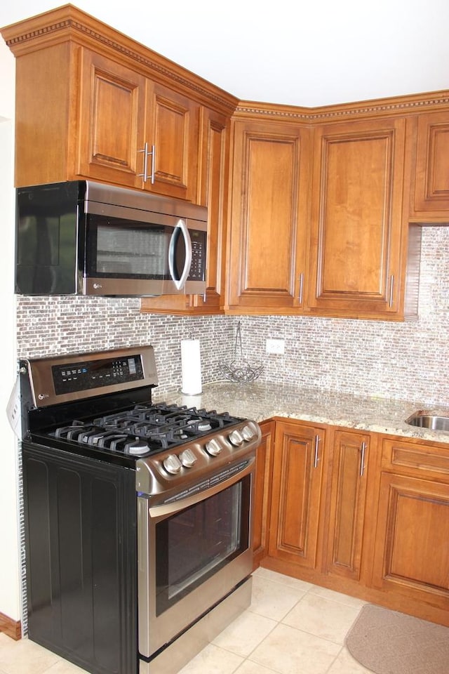 kitchen with light stone countertops, tasteful backsplash, stainless steel appliances, and brown cabinetry