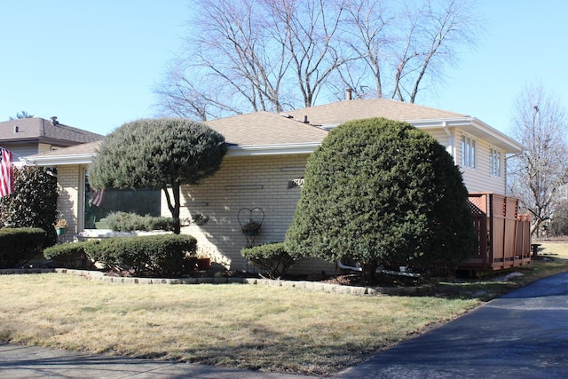 view of side of property featuring brick siding, a shingled roof, and a yard