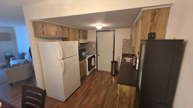 kitchen with gas range, dark wood-style flooring, freestanding refrigerator, under cabinet range hood, and backsplash