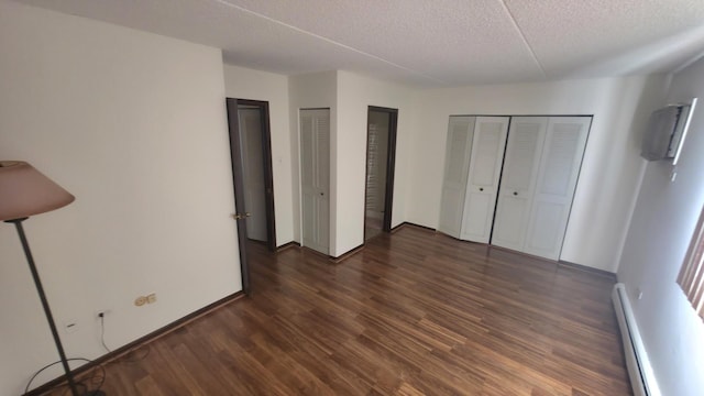 unfurnished bedroom with baseboards, wood finished floors, baseboard heating, a textured ceiling, and two closets