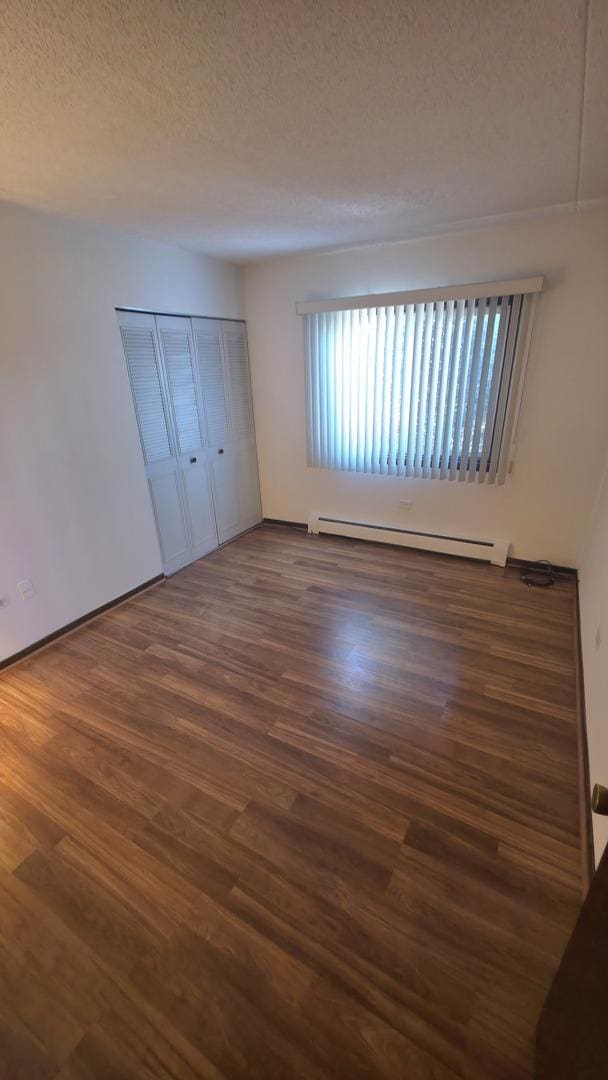 unfurnished bedroom with a baseboard radiator, a textured ceiling, a closet, and wood finished floors