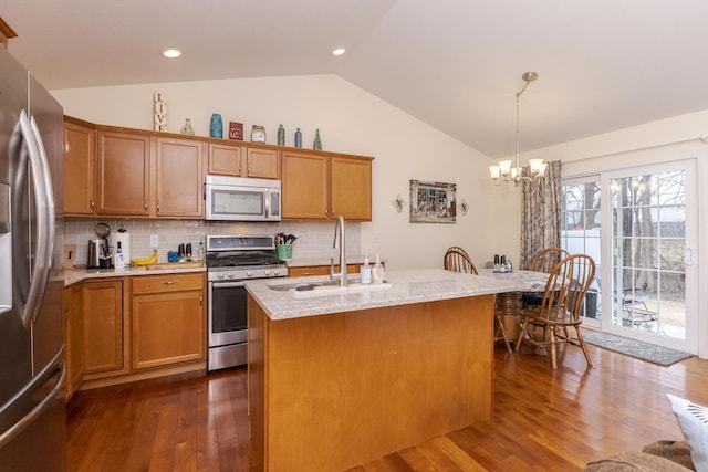 kitchen featuring stainless steel appliances, a sink, vaulted ceiling, hanging light fixtures, and an island with sink