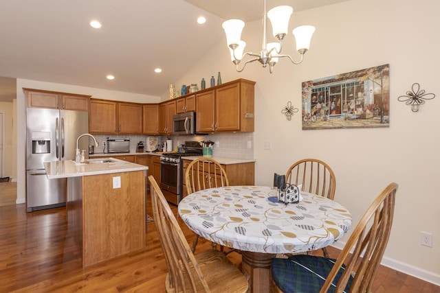 kitchen featuring brown cabinetry, an island with sink, a sink, stainless steel appliances, and backsplash