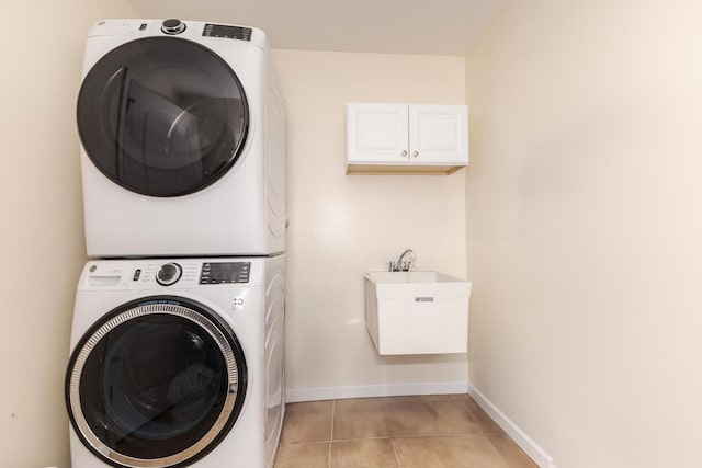 laundry area with light tile patterned flooring, stacked washer / dryer, a sink, baseboards, and cabinet space