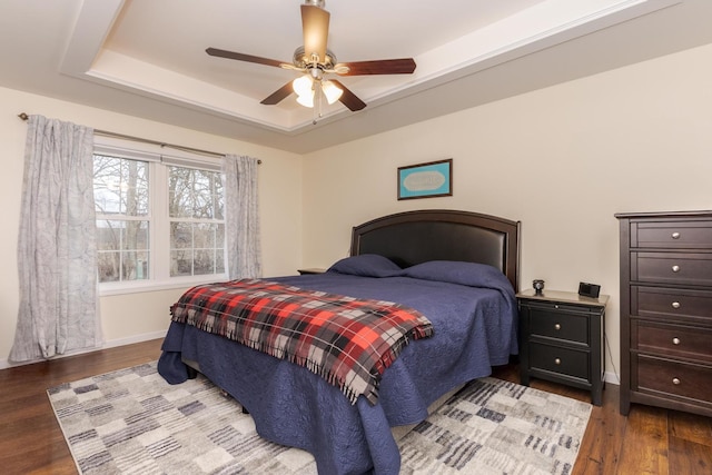 bedroom featuring light wood-style floors, baseboards, a tray ceiling, and ceiling fan