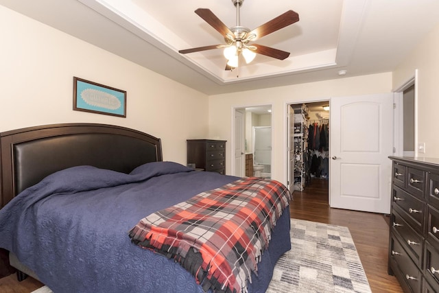 bedroom featuring dark wood finished floors, ensuite bathroom, a spacious closet, a tray ceiling, and a closet