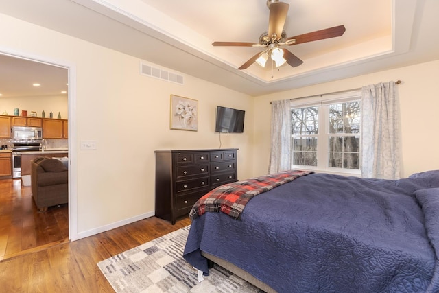 bedroom featuring light wood finished floors, visible vents, baseboards, a ceiling fan, and a tray ceiling