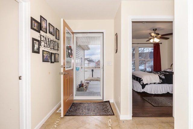 doorway featuring ceiling fan, baseboards, and light tile patterned flooring