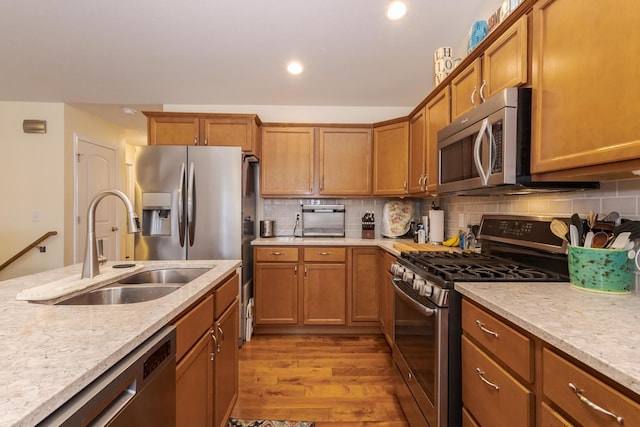 kitchen featuring brown cabinets, stainless steel appliances, decorative backsplash, a sink, and light wood-type flooring