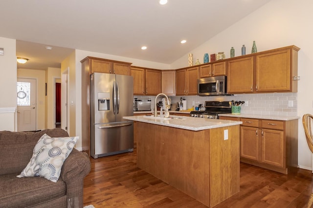 kitchen with brown cabinets, stainless steel appliances, lofted ceiling, open floor plan, and a kitchen island with sink