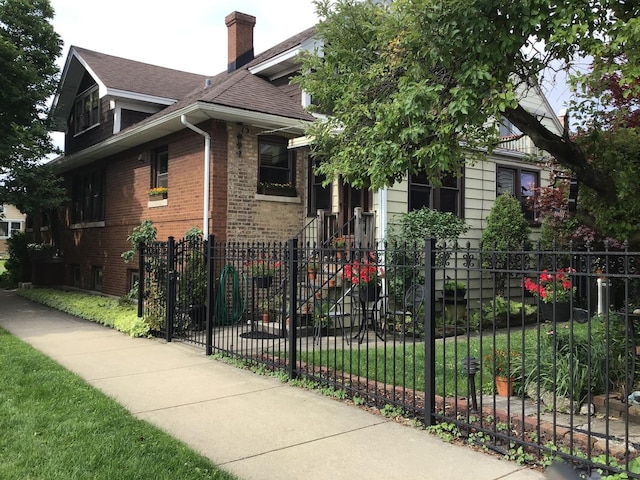 bungalow featuring a fenced front yard, a chimney, a shingled roof, and brick siding