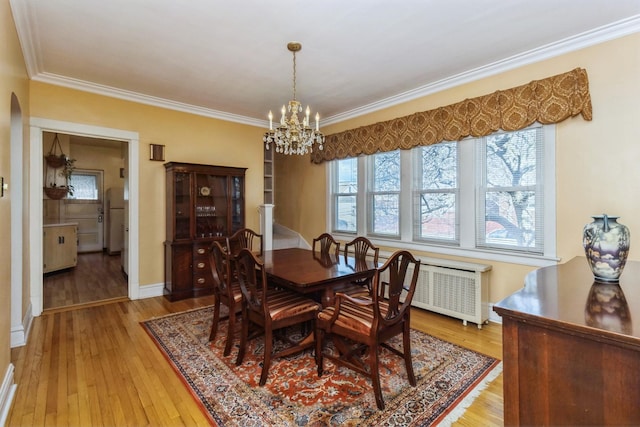 dining space featuring light wood-style floors, arched walkways, ornamental molding, and radiator heating unit