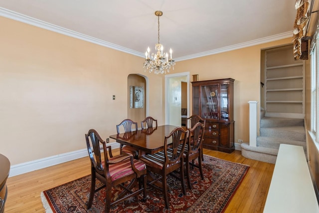 dining room with stairs, ornamental molding, arched walkways, and wood finished floors