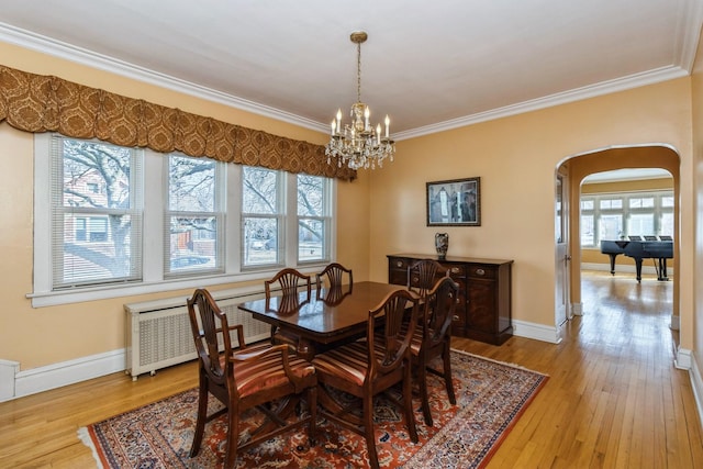 dining area featuring light wood-style floors, arched walkways, a healthy amount of sunlight, and crown molding