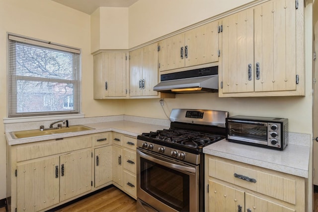 kitchen with under cabinet range hood, stainless steel gas range oven, light countertops, and a sink