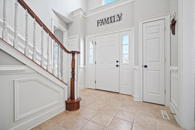 foyer entrance featuring light tile patterned flooring, visible vents, stairway, and a towering ceiling