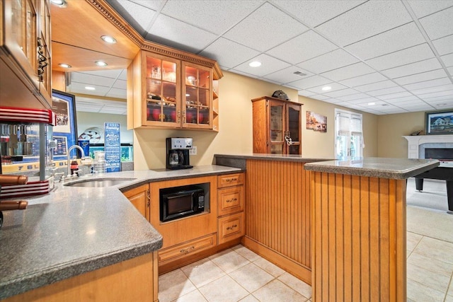 kitchen featuring a peninsula, black microwave, glass insert cabinets, and a sink