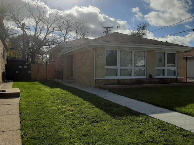 view of side of home featuring a shingled roof, brick siding, a lawn, and fence