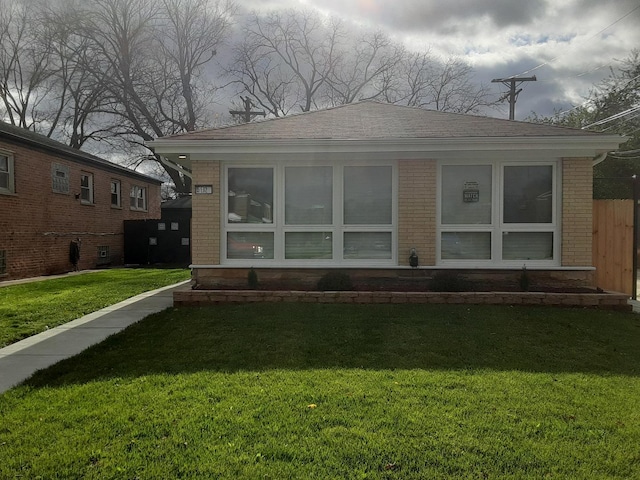 rear view of house with roof with shingles, brick siding, and a lawn