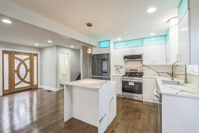 kitchen featuring hanging light fixtures, appliances with stainless steel finishes, white cabinets, a sink, and a kitchen island