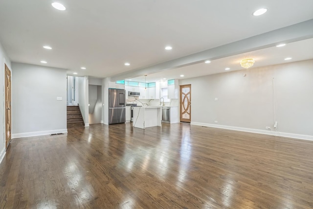 unfurnished living room with dark wood-style floors, baseboards, a sink, and recessed lighting