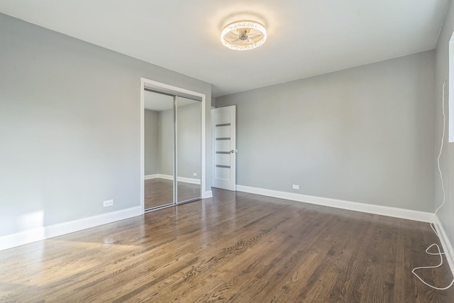 unfurnished bedroom featuring dark wood-type flooring, a closet, and baseboards