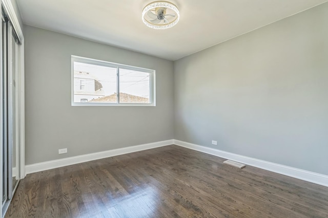 empty room with baseboards, visible vents, and dark wood finished floors