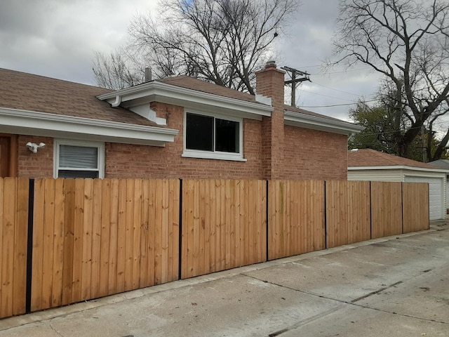 view of property exterior featuring brick siding, fence, and a chimney