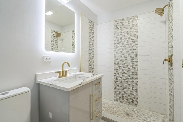 bathroom featuring a tile shower, vanity, and toilet