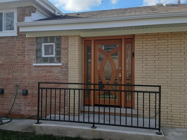 doorway to property with a shingled roof and brick siding