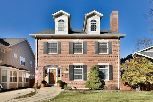 view of front of house with a front yard, a chimney, and brick siding