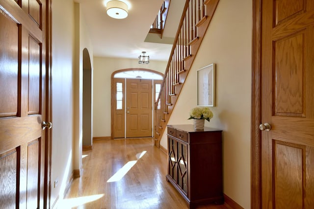 entrance foyer with arched walkways, light wood-style flooring, baseboards, and stairs