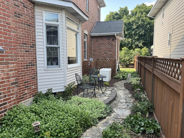 exterior space featuring a shingled roof, a patio area, brick siding, and fence